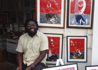A proud artist with his work - George Ongeri beams alongside his masterpieces at his shop, The Art Kiosk