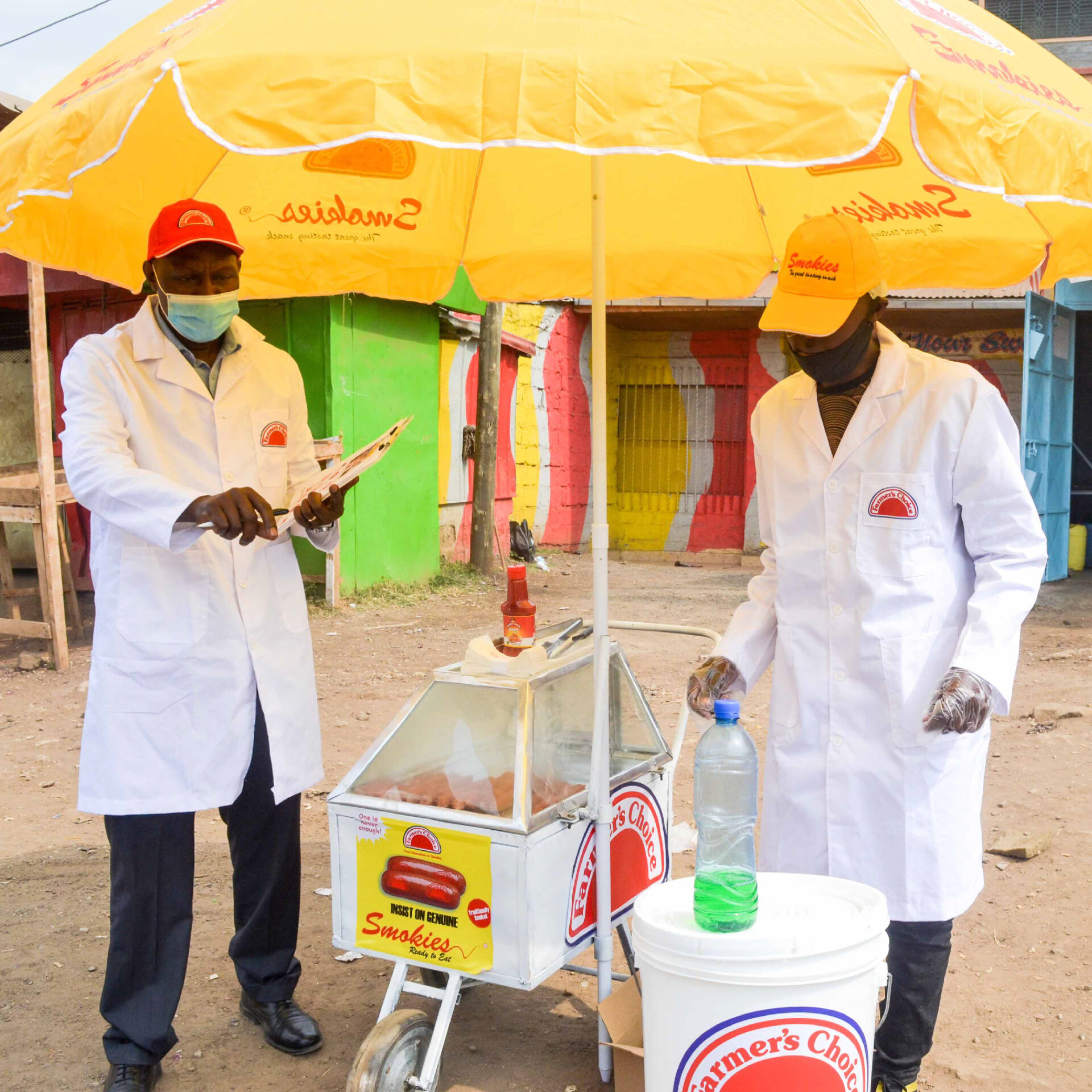 Two men dressed in caps and white aprons manning a Farmers Choice Smokie Trolley